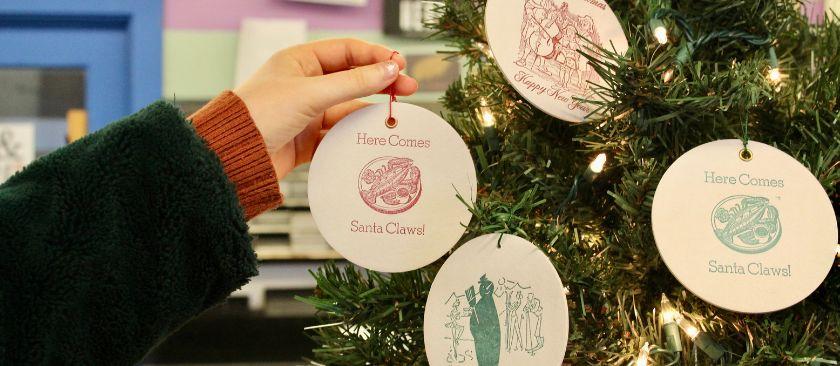Close-up of a hand reaching out to hang up a wooden holiday ornament on a tree.