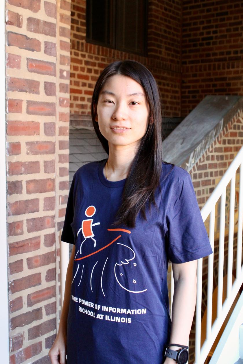 PhD student Meng Li wears her winning design for the iSchool T-shirt contest. The design show a stylized sketch of a figure surfing.