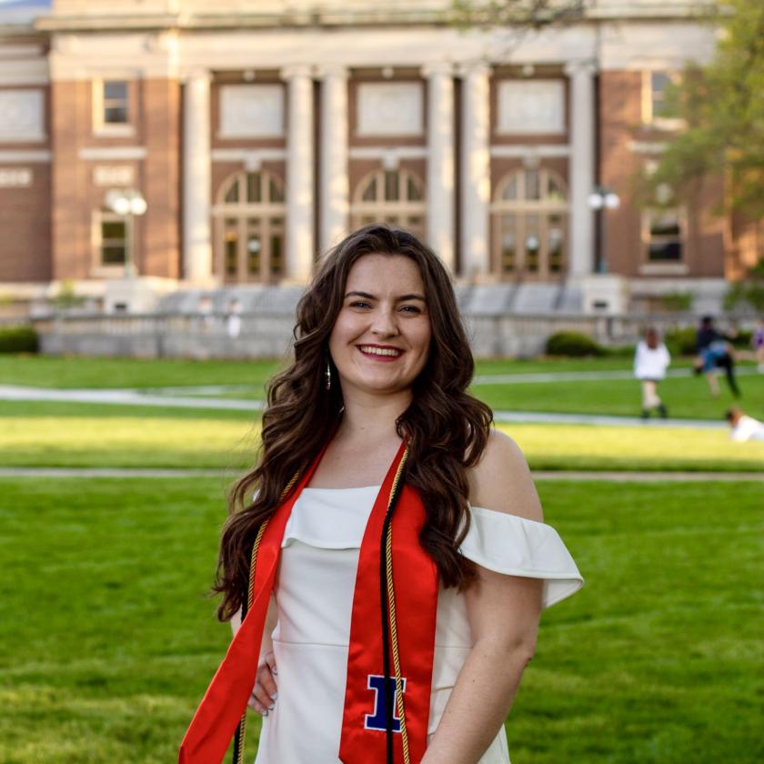 Nicole Angell wearing her graduation stole and smiling in front of Foellinger Auditorium.