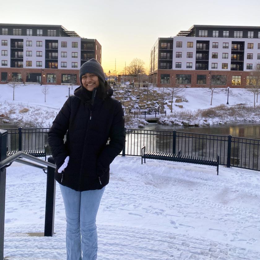 Payal Narvekar stands on snow-covered steps, with a lake and buildings in the background