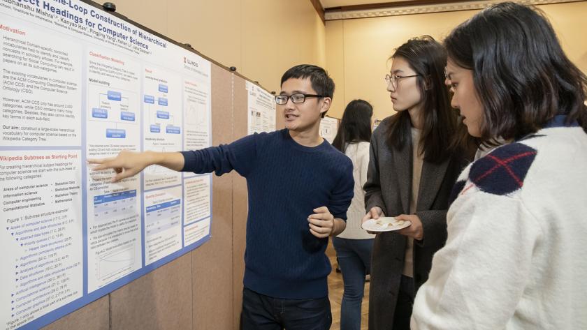 a student describes his poster to other students at a past research showcase