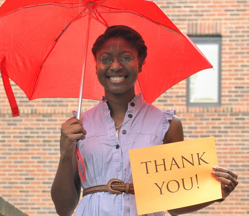 female student under umbrella holding thank you sign