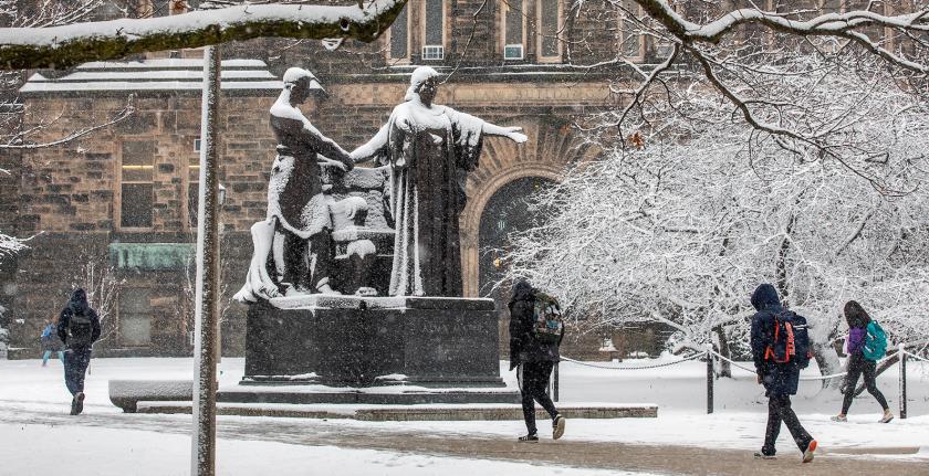 students walk in front of Alma Mater on snowy day
