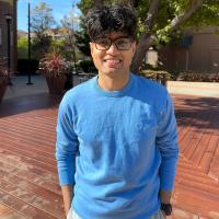 Tan Debnath stands casually with his hands in his pockets and smiles broadly at the camera. It's a sunny day